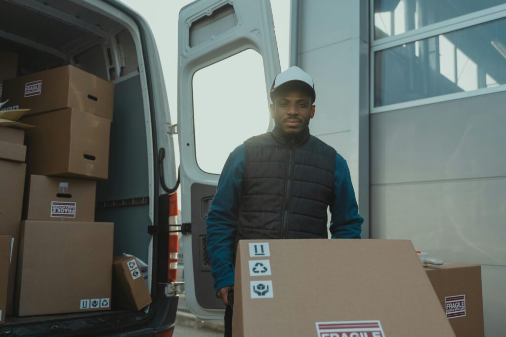 Picture of man carrying box on cart out of a back of a van, walking towards the viewer.